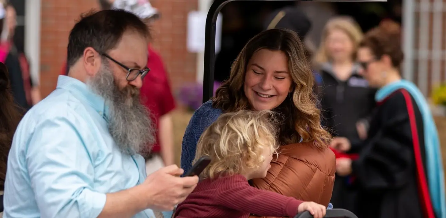 Two adults and one toddler sitting in a golf cart, smiling together at graduation