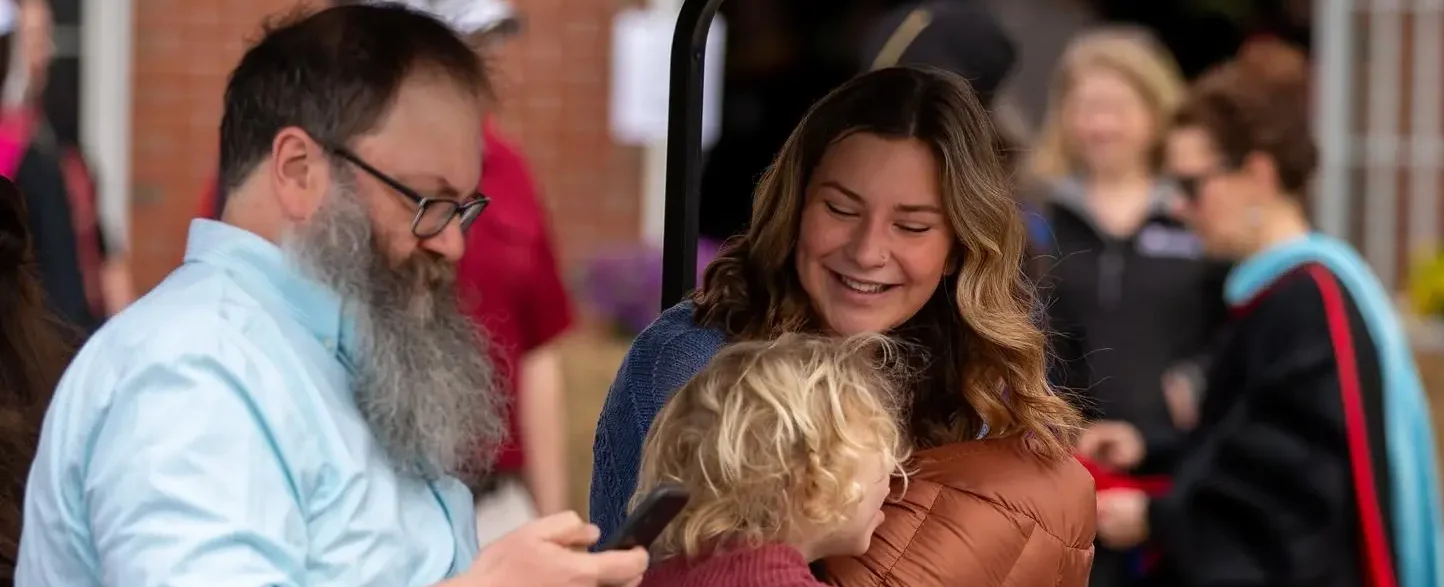 Two adults and one toddler sitting in a golf cart, smiling together at graduation