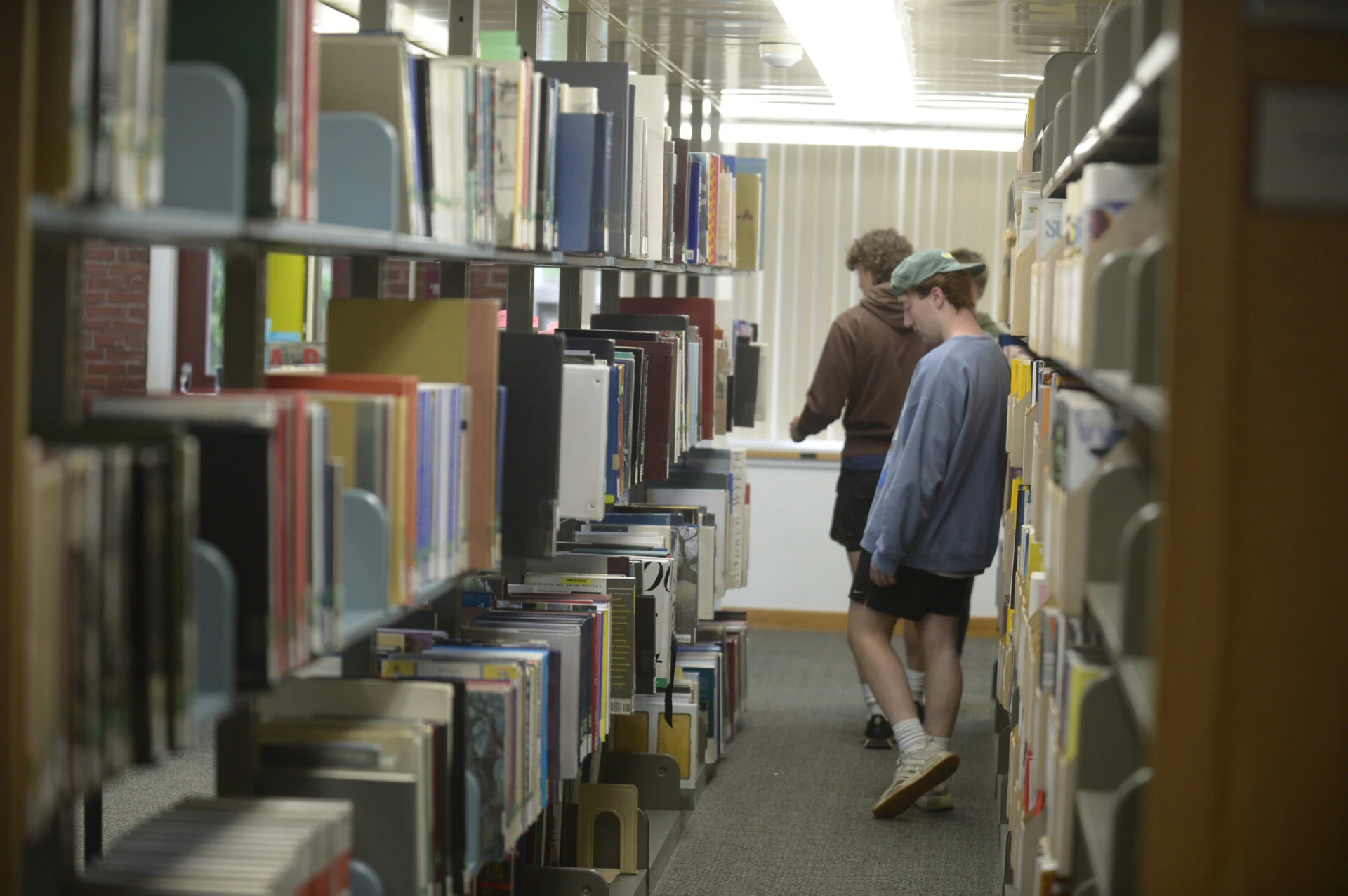 UMF students stroll through row of books in the Mantor Library.