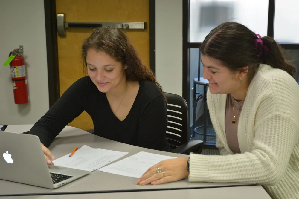 Two people sitting at a table together looking at a laptop.