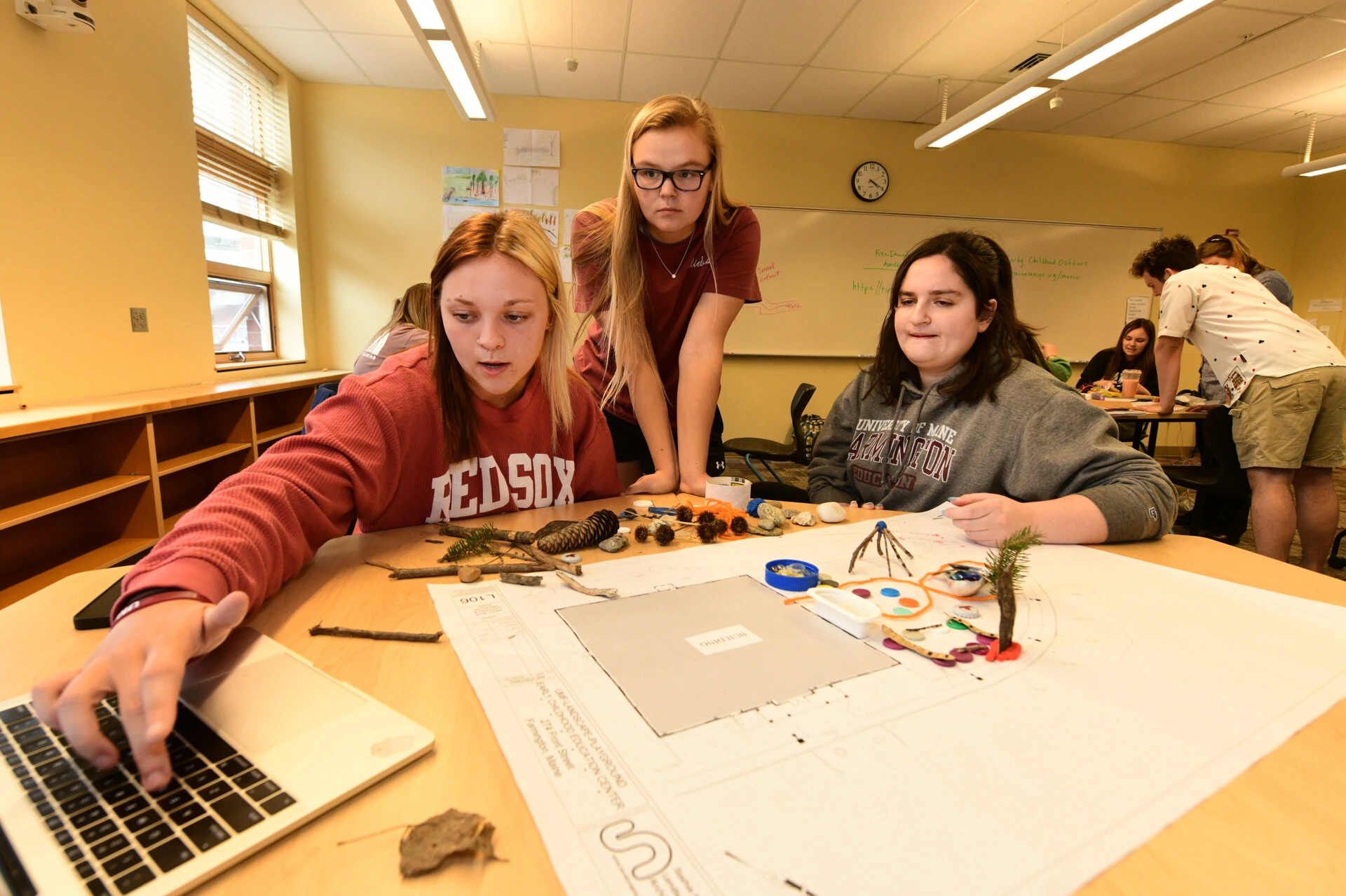 Three female students in a classroom working on a project while using a laptop