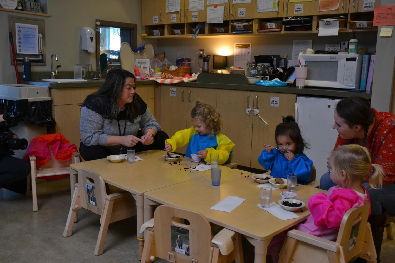 UMF Graduate students sits at classroom table with young children.