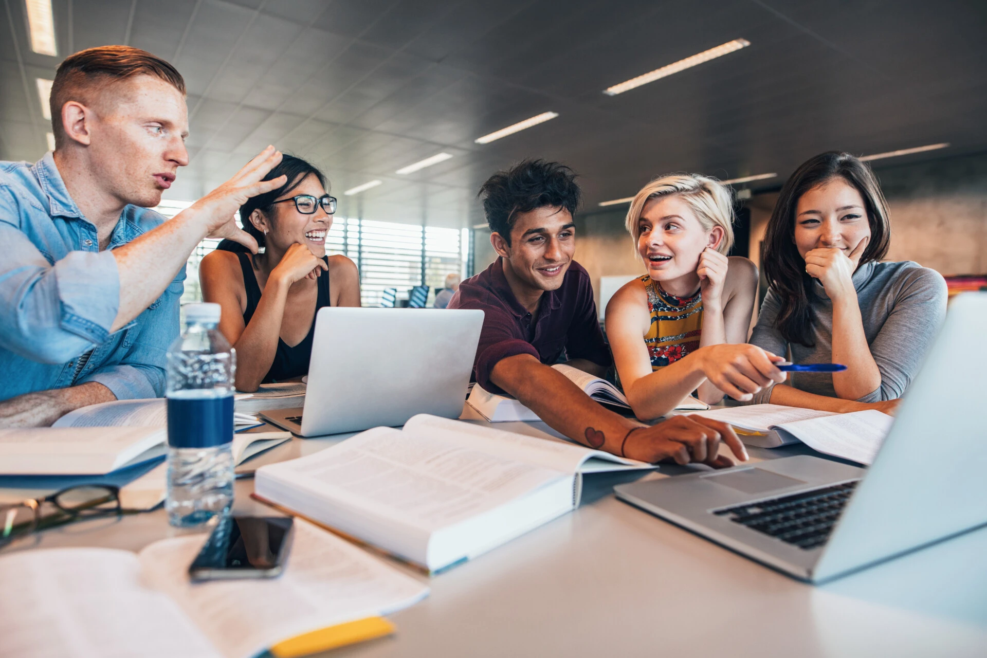 Diverse group of students working together at a large desk with papers and laptops