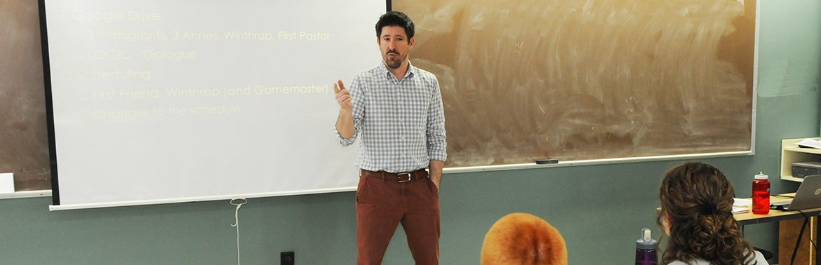 History professor stands at front of classroom teaching.