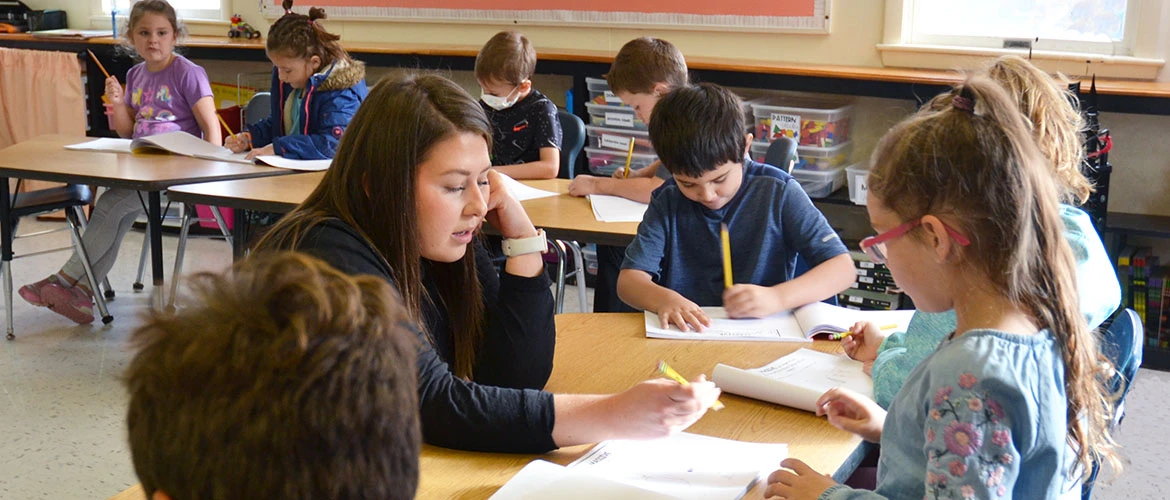 Elementary Education students works with group of children at desk.