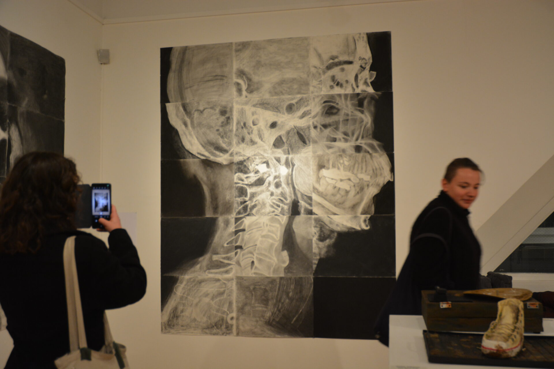 A guest photographing a student's gallery piece of an x-ray of a human head.