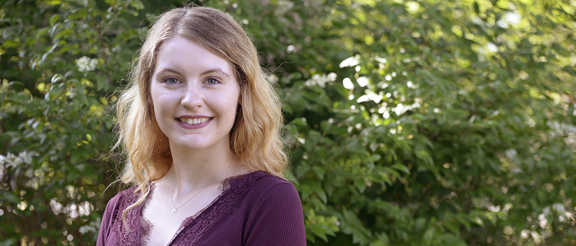 Student smiling at camera with foliage behind them.