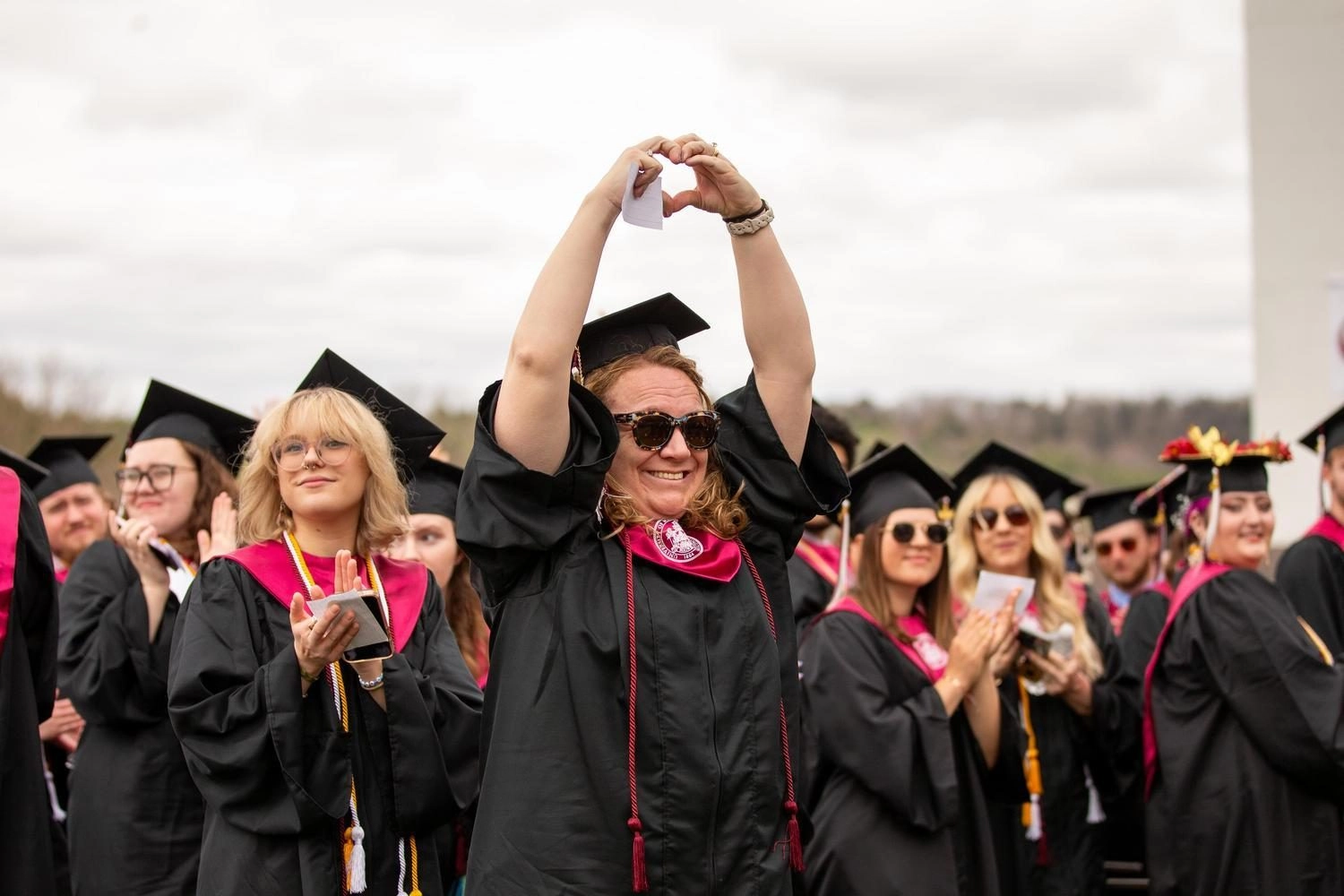 Graduate raises arms into a hand shape at commencement ceremony