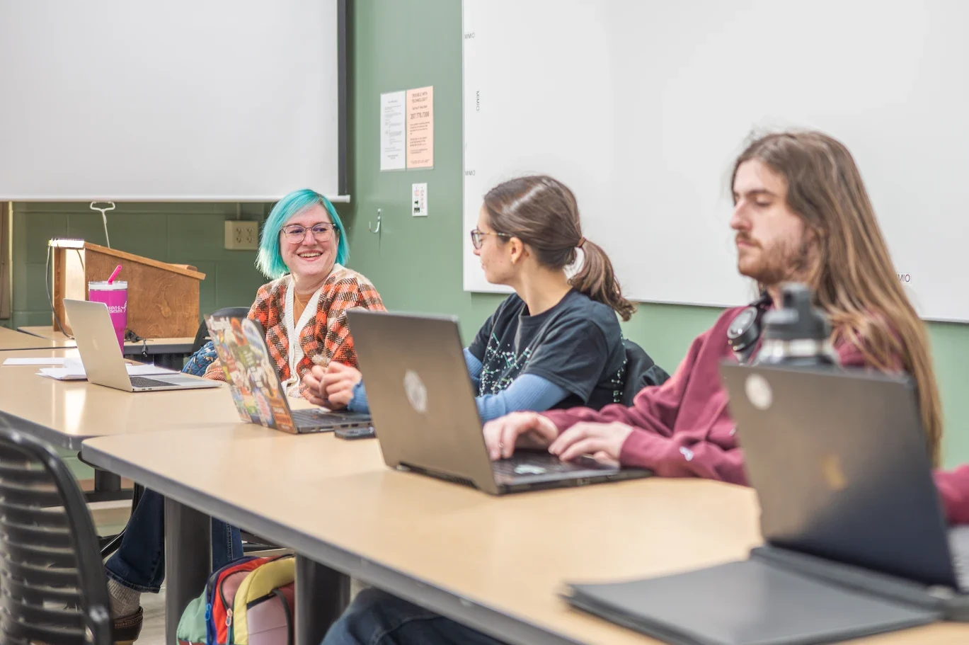 Teacher and students sitting at a desk in front of computers