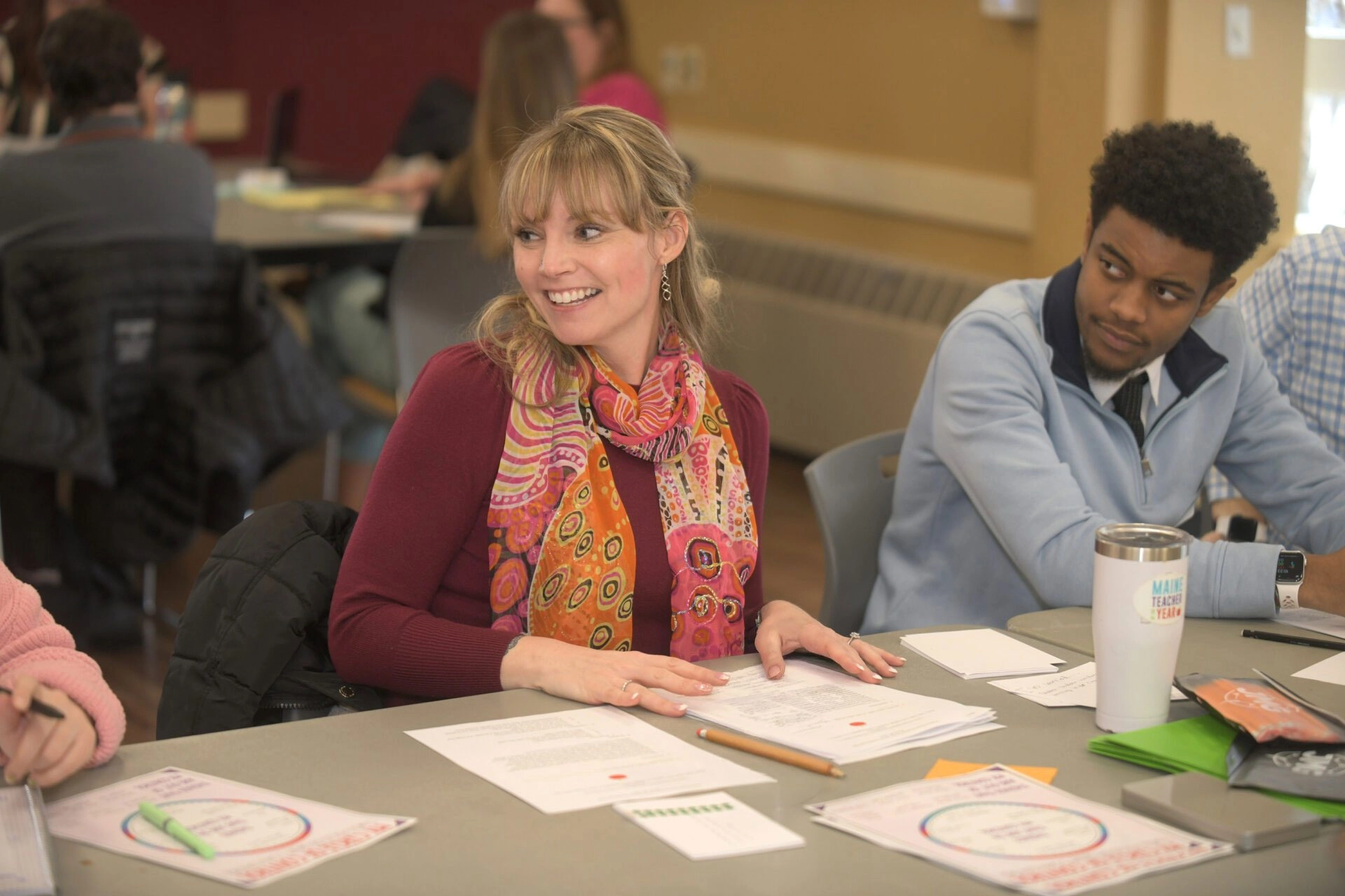 Students sitting at a table smiling and looking at each other