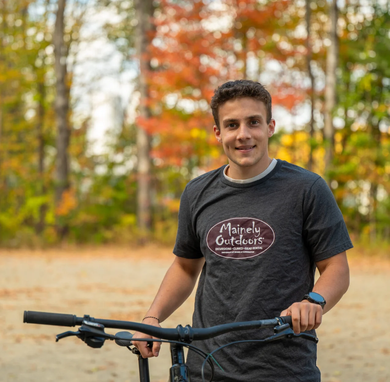 Image of a Mainely Outdoors staff member standing next to a bike in front of trees in fall