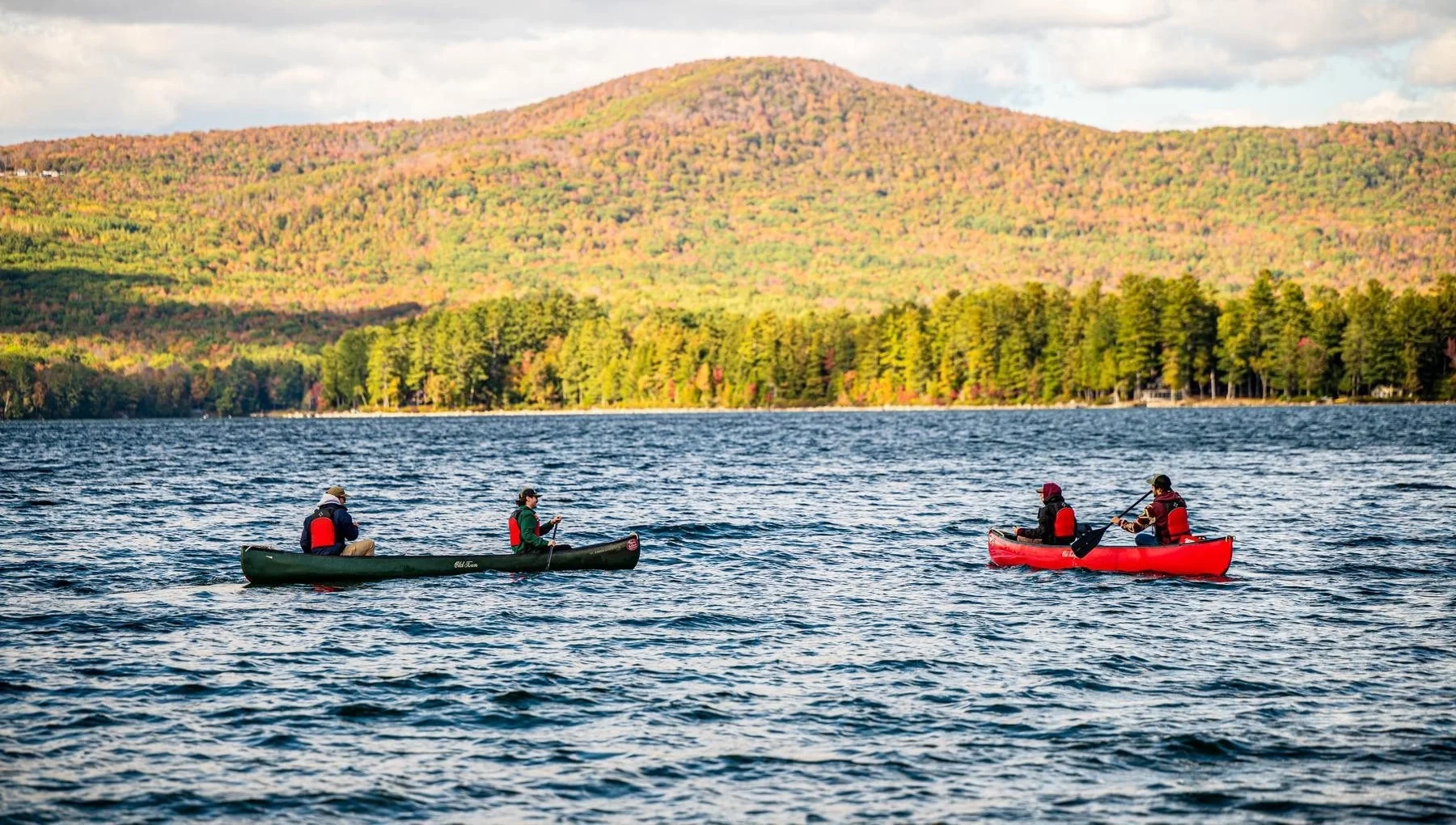 Two canoes on a lake in front of mountains on a fall day.