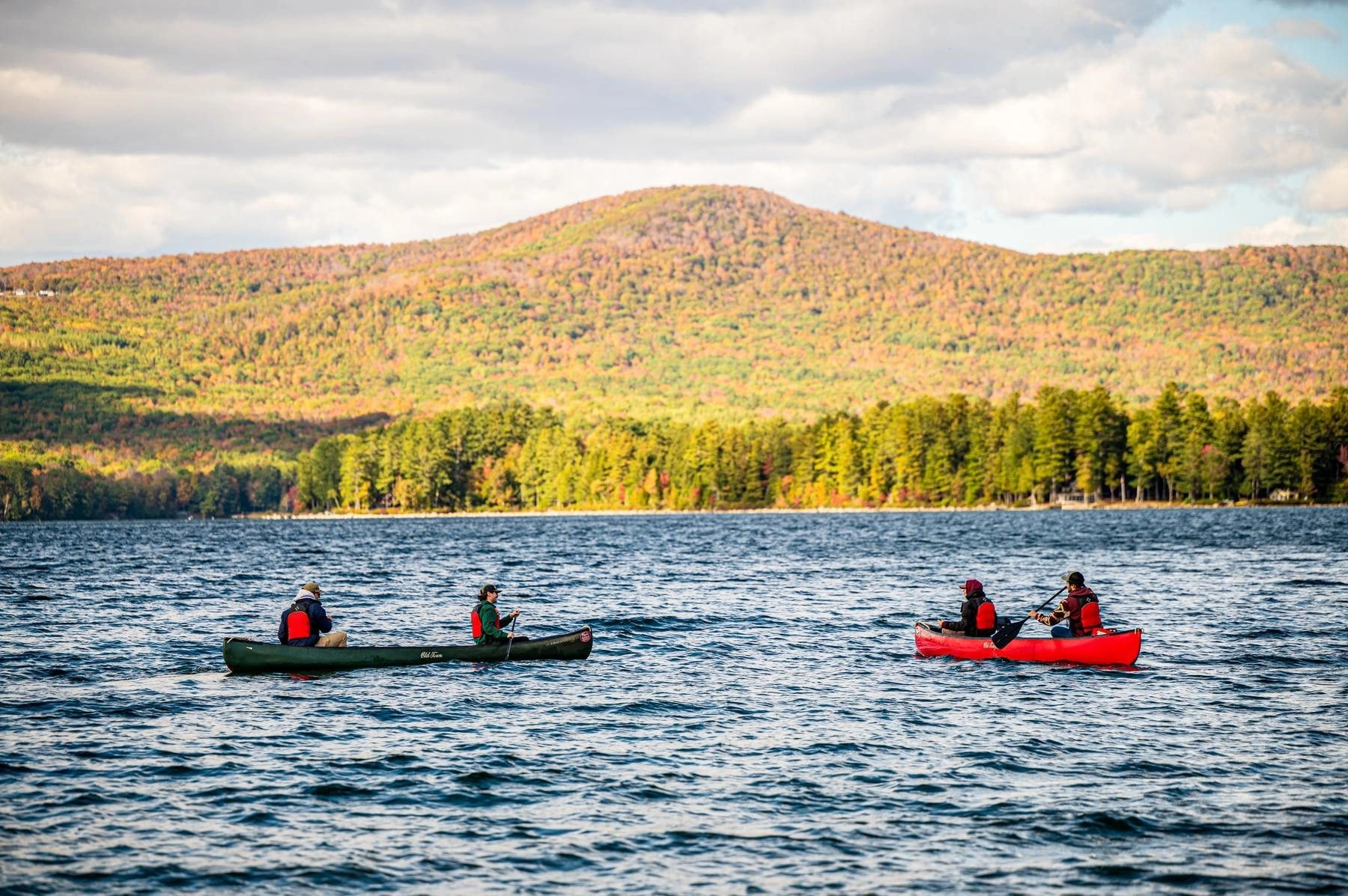 Two canoes on a lake in front of mountains on a fall day.