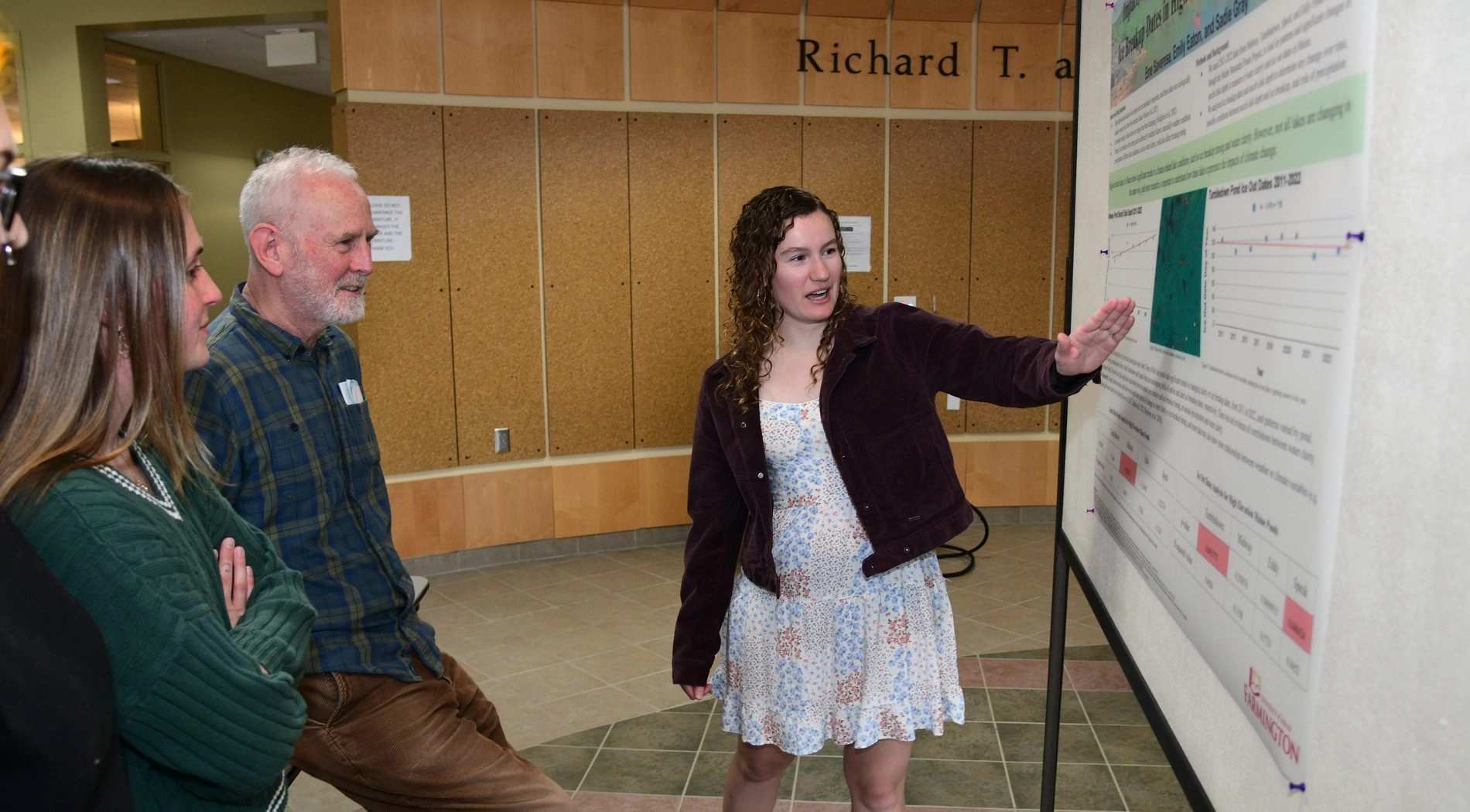 Student demonstrating poster research to group of individuals.