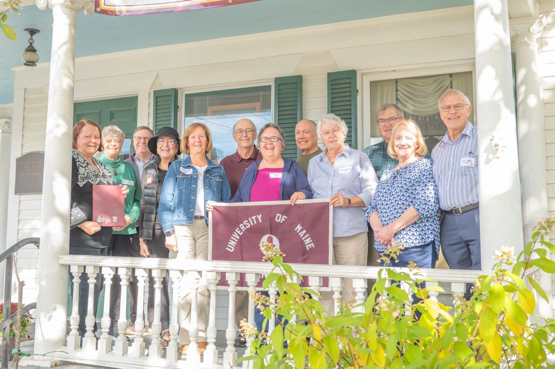 Alumni standing on a porch with a University of Maine banner