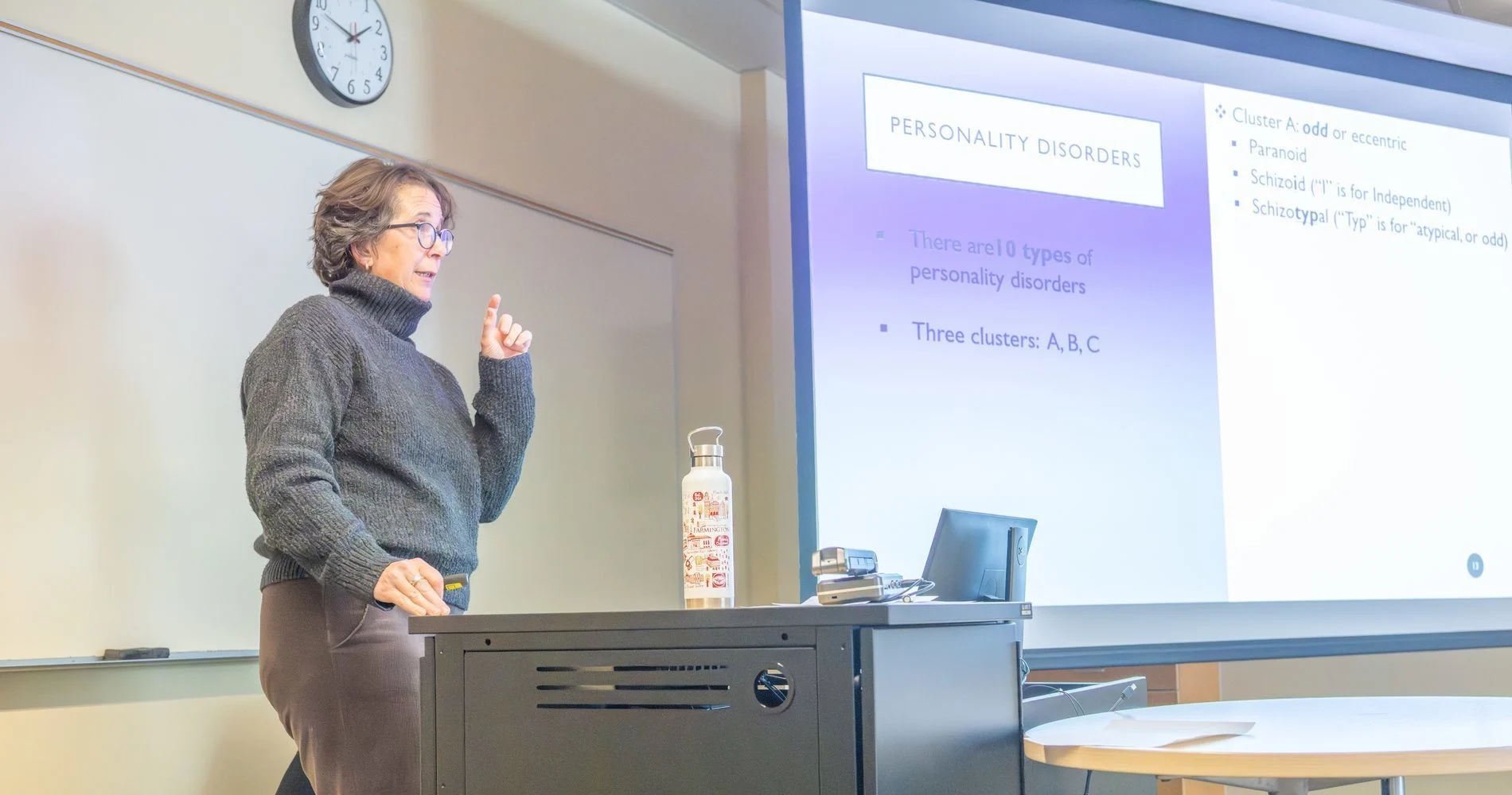 Professor teaching a psychology class in the front of the classroom next to a screen