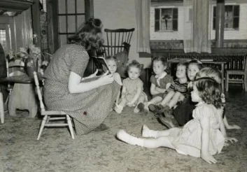 Black and white image from 1940 of a teacher reaching in front of children
