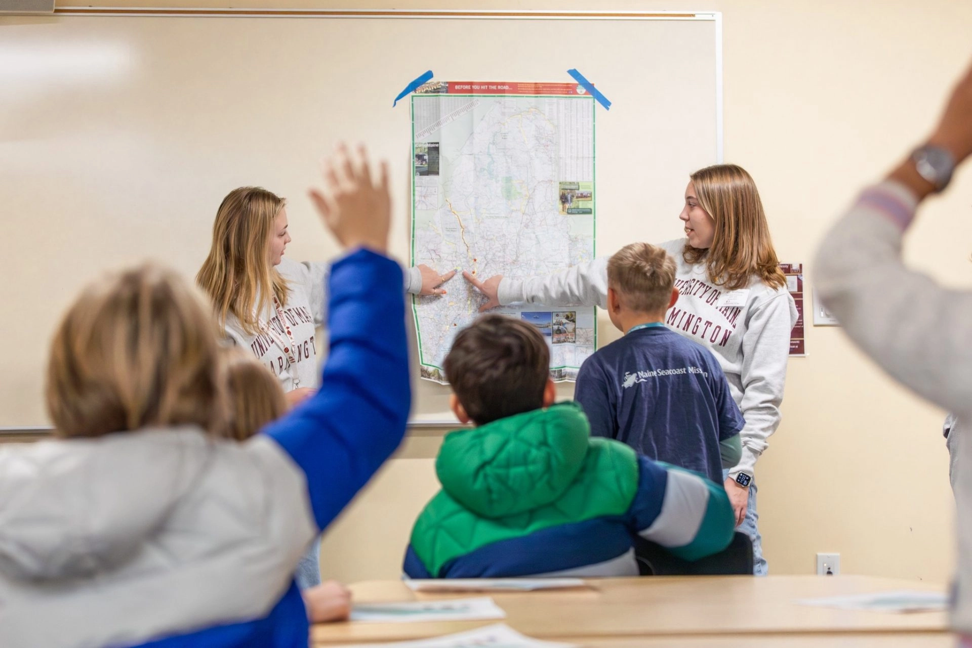 Two student teachers in front of students in classroom pointing the board