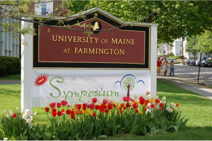 External image of university of maine sign with a symposium banner below and flowers blooming.