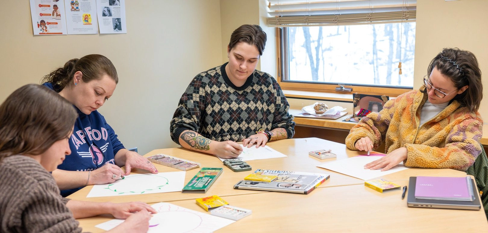 Image of four students sitting at a desk creating art