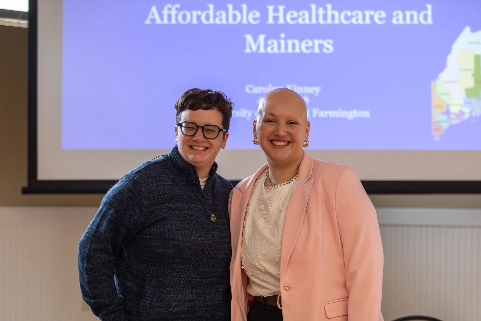 Two students smiling in front of a presentation screen that says 