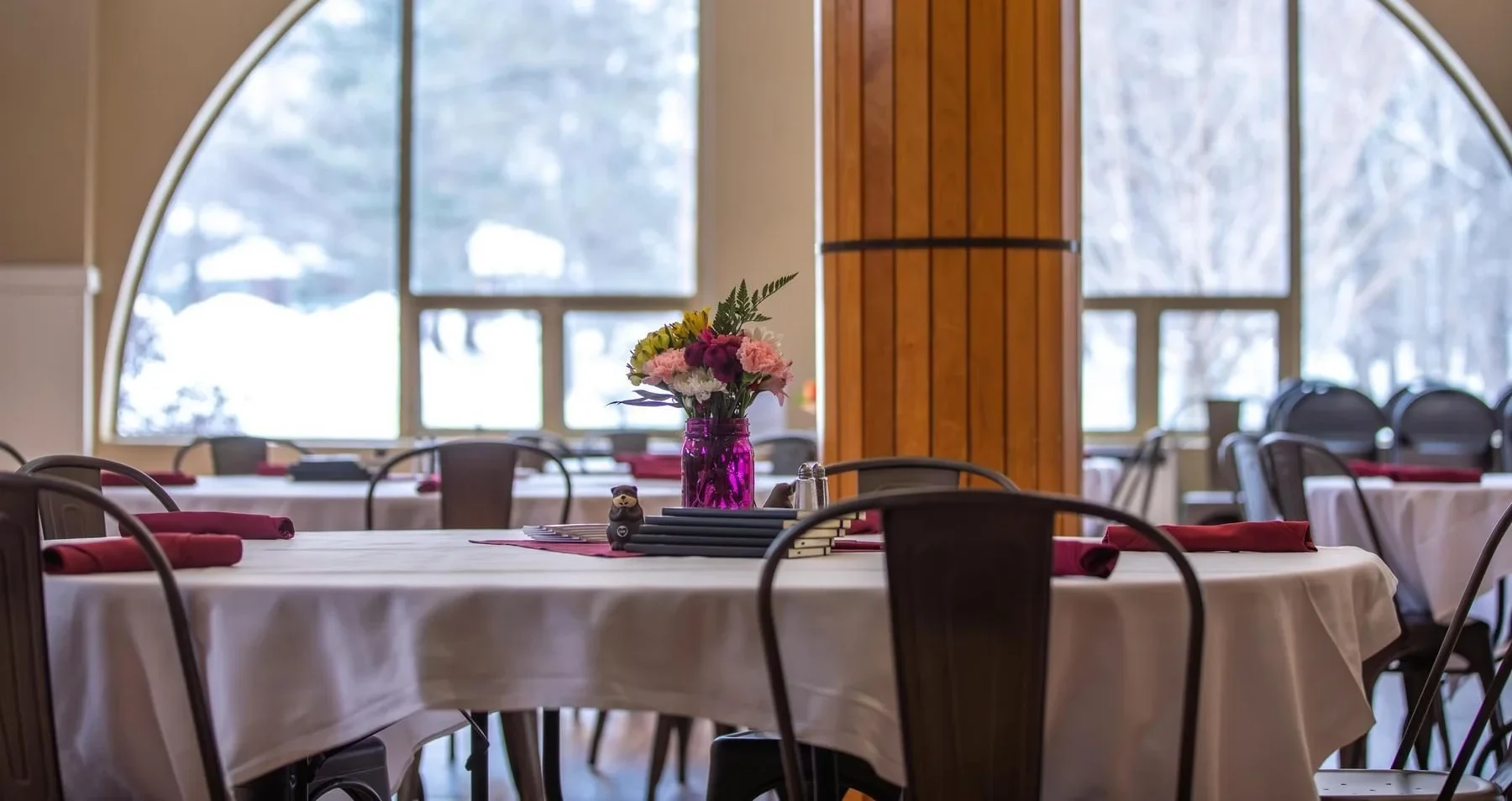 Interior image of tables set up with napkins and white tablecloth with flowers and swag in the middle.