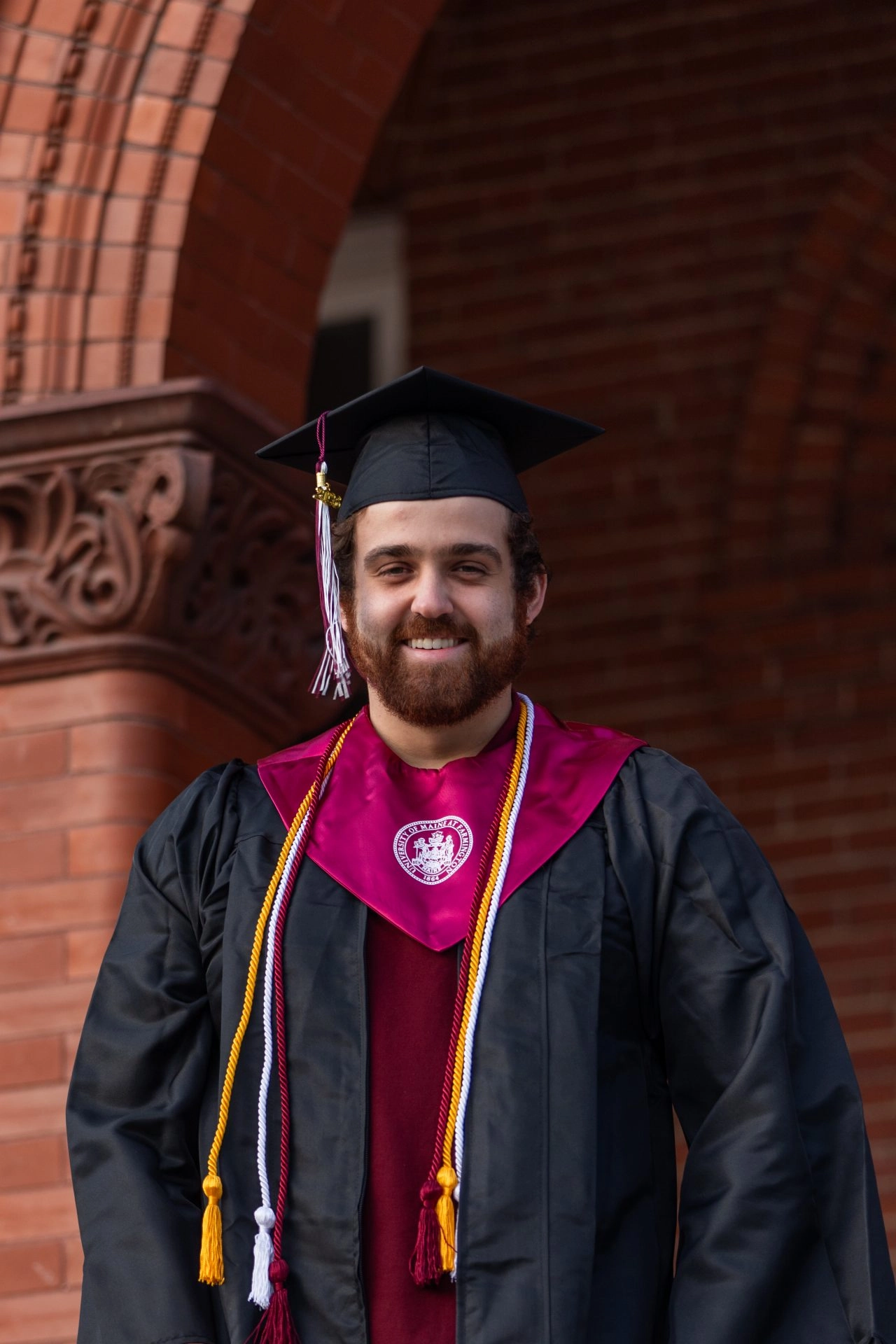Smiling student in regalia in front of brick building outside