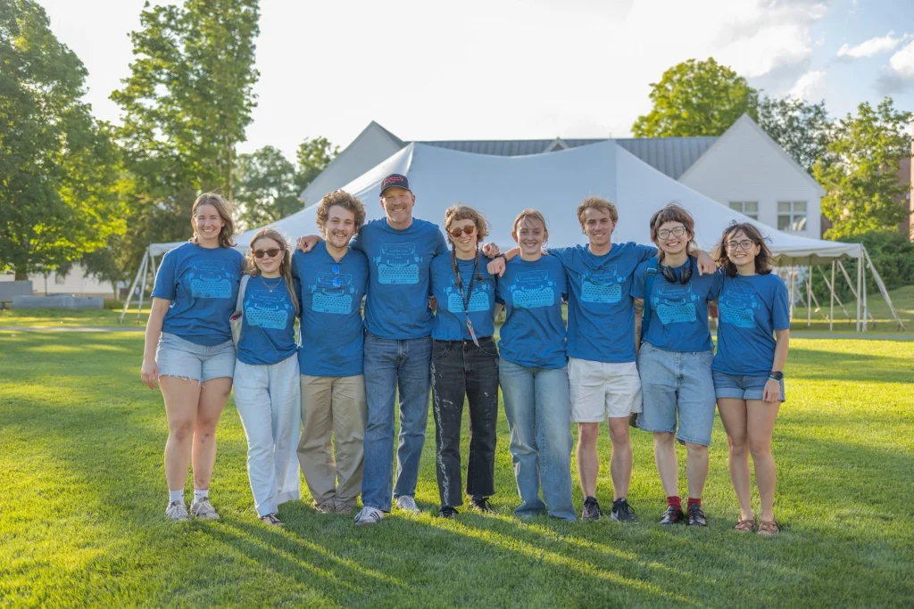 Nine happy UMF Longfellow Camp counselors standing arm-in-arm on the UMF campus green.