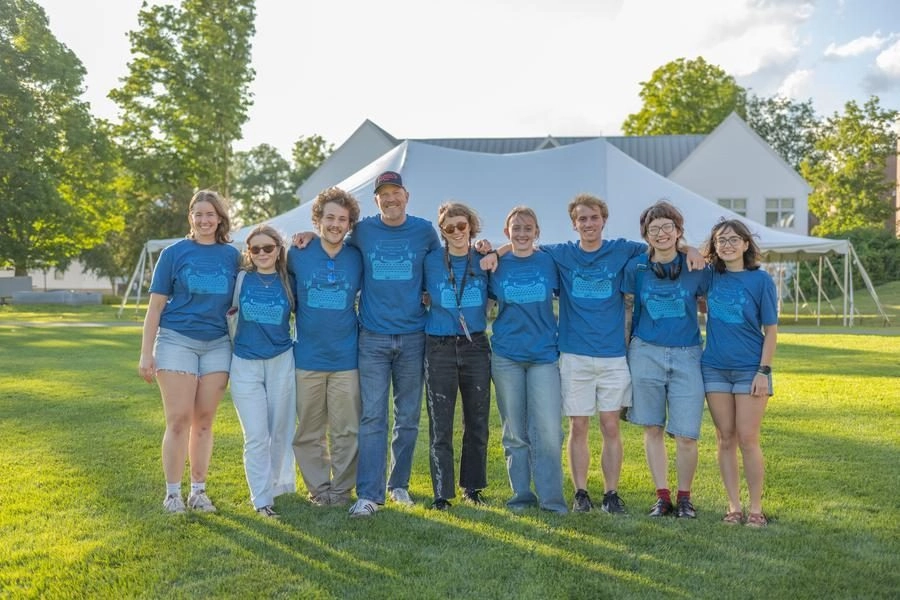 Group of people wearing matching blue shirts posing together on a sunny lawn with a large white canopy in the background.