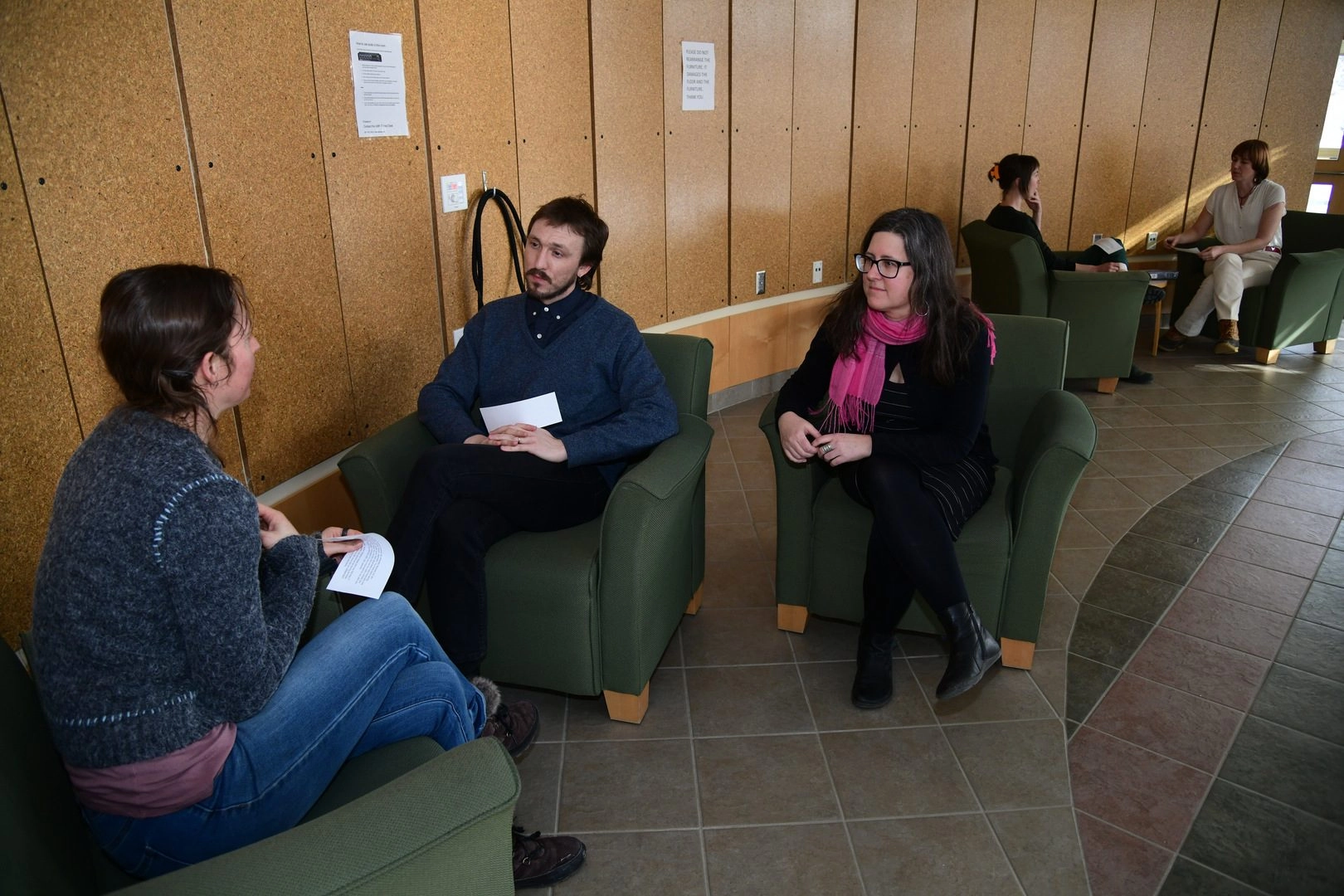 Students sitting in chairs talking with a professor advising next to them.