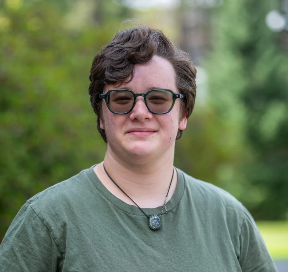 Smiling student with sunglasses and necklace against a natural background