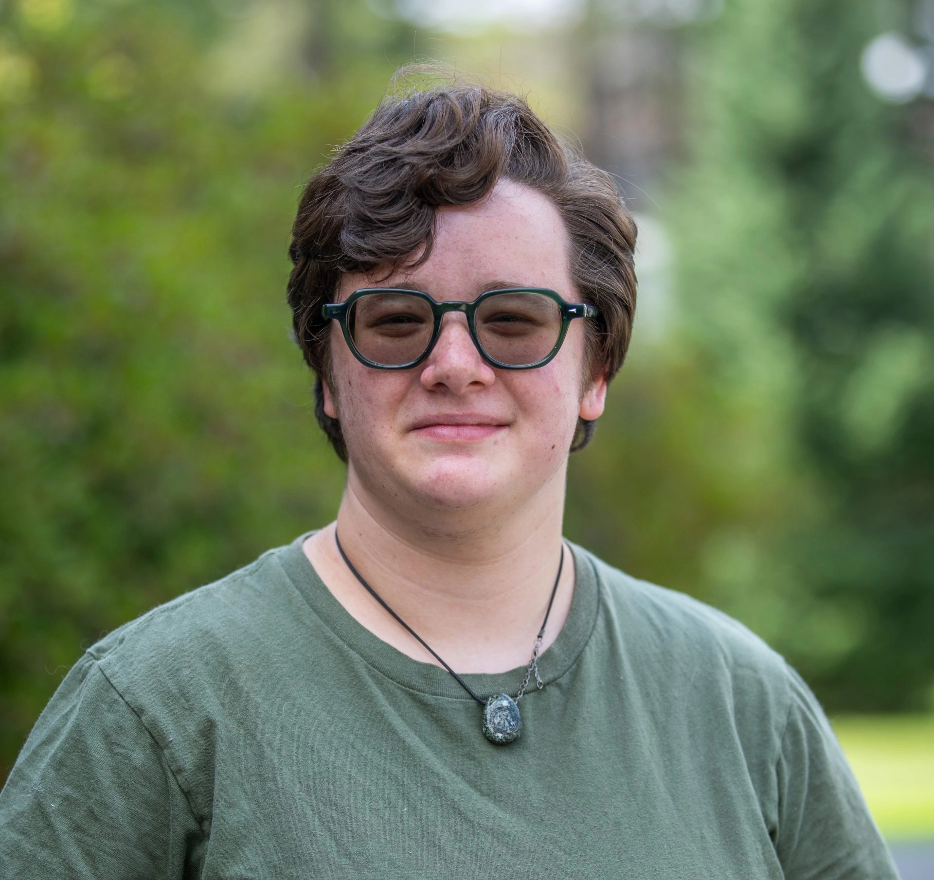 Smiling student with sunglasses and necklace against a natural background
