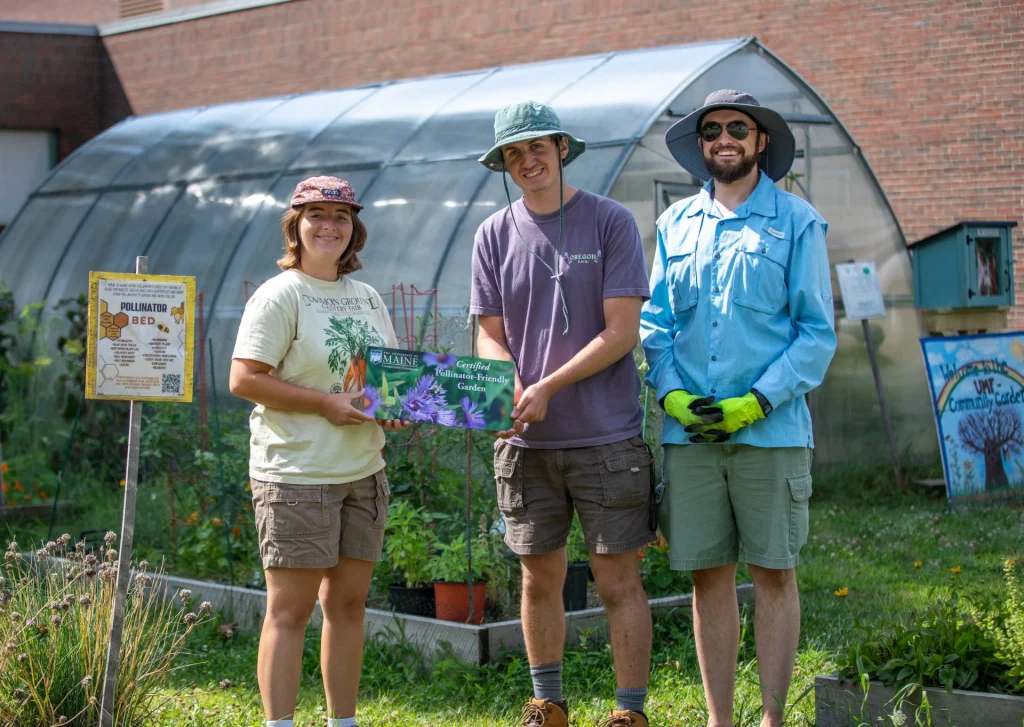 Smiling student garden workers and garden director sharing "Pollinator-Friendly Garden" plaque'