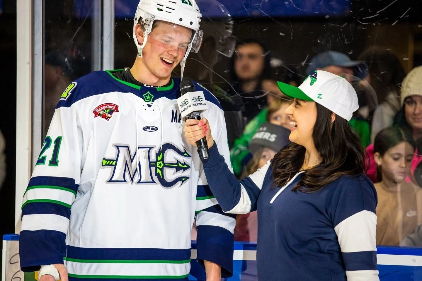 Hockey player in white jersey #21 smiles during an interview with a reporter holding a mic.