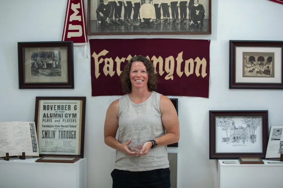 Smiling woman holding a glass award in a room with framed vintage photos and a maroon banner behind her