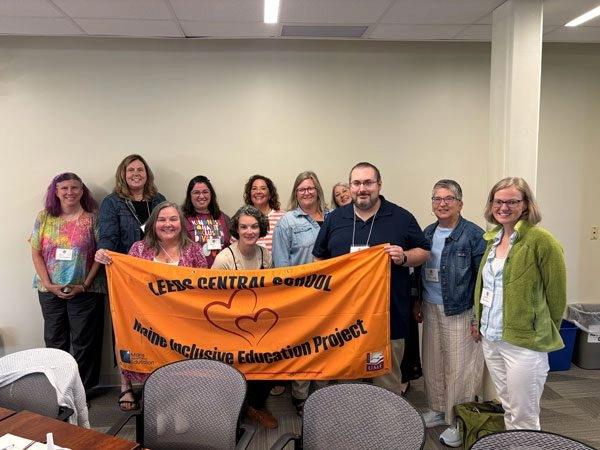 Group of adults in a meeting room holding an orange banner with a heart for the Inclusive Education Project.