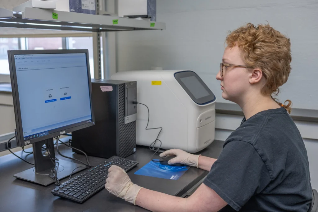 Woman with glasses and red hair working at a computer screen in the biology lab